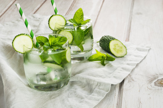 Homemade lemonade. Water with cucumber,mint  and ice in glass on a white wooden background. Rustic style.