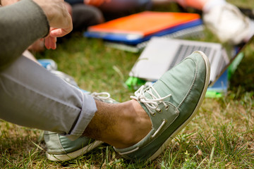 Close up view on mans leg in moccasins. Boy in blue moccasins sitting on grass.