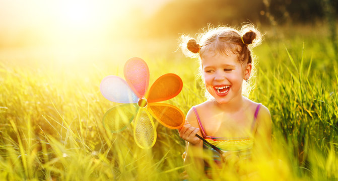 Happy child girl with colorful pinwheel windmill in summer