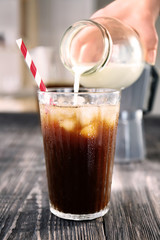 Pouring milk into glass with cold brew coffee on wooden table