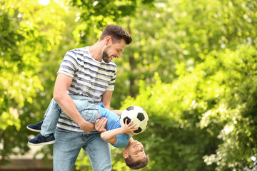 Naklejka premium Dad and son with soccer ball in green park