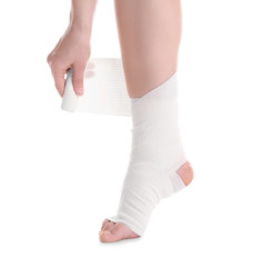 Young woman applying bandage onto leg, on white background