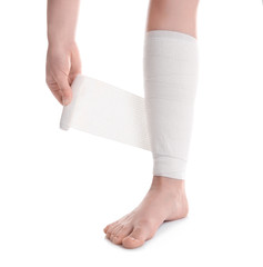 Young woman applying bandage onto leg, on white background