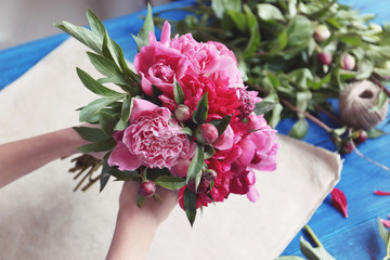 Female florist making bouquet of beautiful peonies in flower shop, closeup