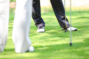 Legs of young men playing golf on course in sunny day