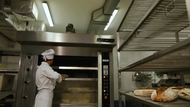 Baker man in the uniform taking breads from oven and putting it to the reck with other breads. Close up shot.