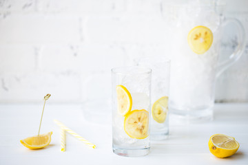 Empty Glasses on the White Brock Wall Filled with Ice and Lemon Slices with Pitcher on the Back