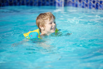 Fototapeta na wymiar Happy blonde boy wearing floaties and swimming in pool