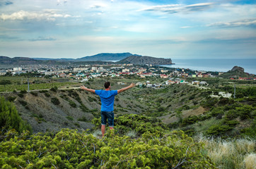 Fototapeta na wymiar A man on the edge of a ravine overlooking the sea, mountains and city