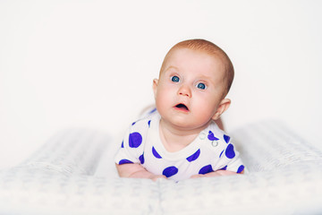 Funny cute baby in clothes with purple peas for the first time raised her head. Amazed baby with a curious look around herself.