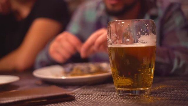 A young man is drinking beer in a bar with dluzyami. Close-up of light beer with foam. In the background, the guy has capelin. Fried appetizing fish in hands.The hand stretches the menu with the score