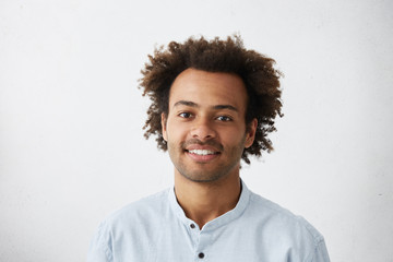 Headshot of good-looking positive young dark-skinned male with stubble and trendy haircut wearing...