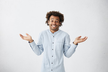 Portrait of uncertain careless young African-American employee wearing long shirt shrugging...
