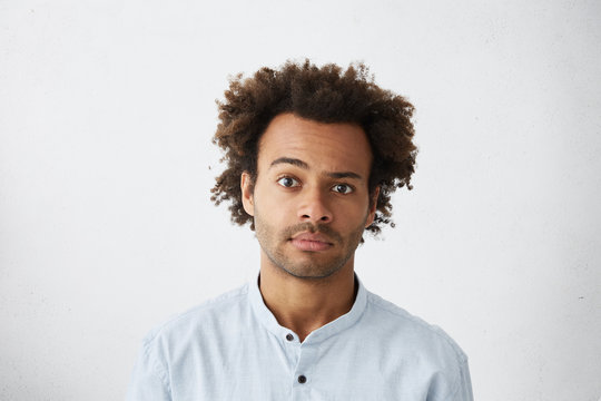 Handsome sceptical unshaven African American office worker wearing blue shirt posing in studio raising one brow, his look full of doubt and distrust. Human emotions, reactions, feelings and attitude