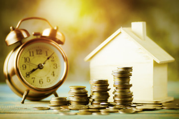 pile of money, coins  growing up with house wood and alarm clock, concept in business about loan, selling,finance, mortgage and buying home