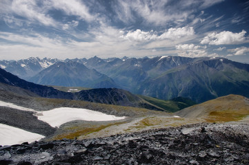 Mountain slope with rocks and snow on the background mountain valley and high snow-capped peaks with glaciers under a bright blue sky with white clouds Altai Mountains Siberia, Russia