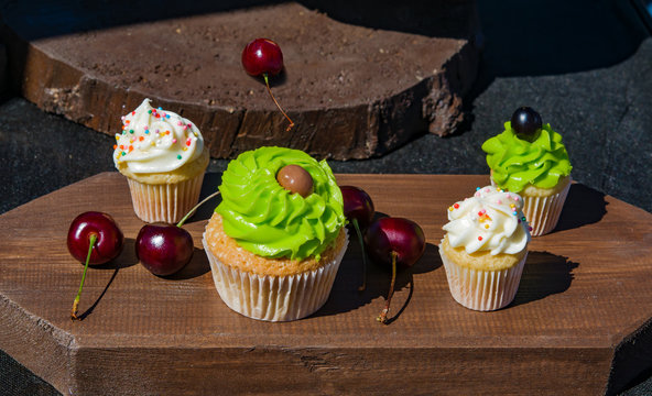 Cakes with green and white cream with berries currants and cherries on a dark wooden board vintage