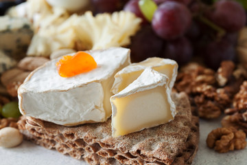 Fototapeta na wymiar Cheese plate served with grapes, jam, cured melon, crackers and nuts