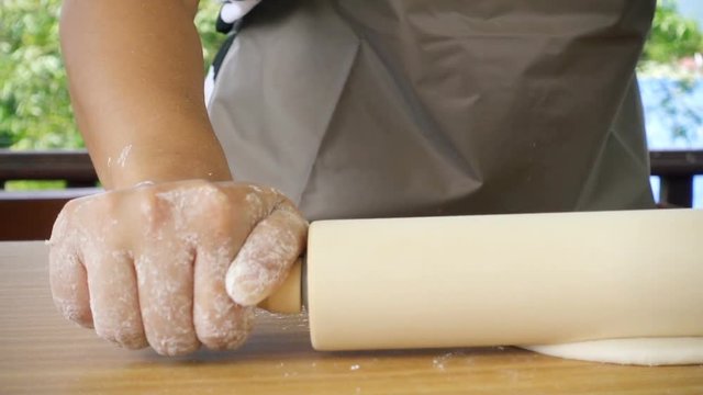 Close-up of female hand rolled fresh dough on the table in slow motion shot