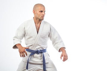A young bald man in a white kimono and blue belt for a kimono, sambo, jiujitsu stands in a fighting...