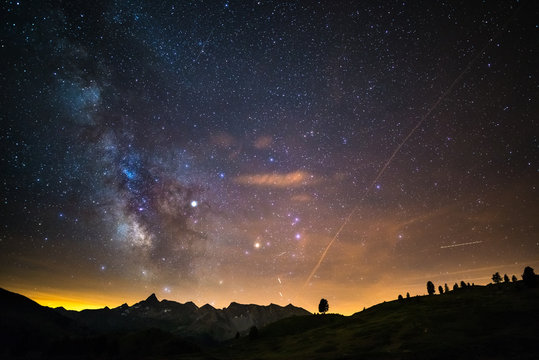 The colorful glowing core of the Milky Way and the starry sky captured at high altitude in summertime on the Italian Alps, Torino Province. Airplane traffic in the sky.