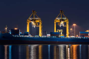 Obraz premium container cargo freight ship with working crane bridge in shipyard at night