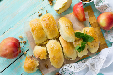 Homemade apple pies with fresh apples and walnuts from yeast dough on a kitchen wooden table. Flat lay, top view with copy space.