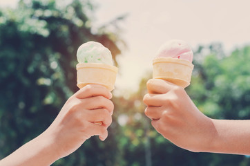 children's hands holding ice cream cone on summer light nature background