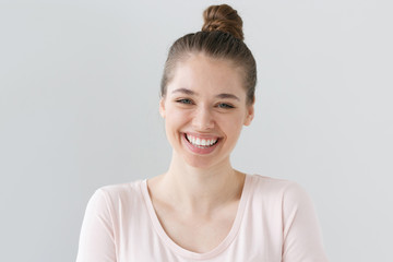 Closeup of positive teenage girl with brown hair tied in bun isolated on gray background with expression of happiness on face, laughing emotionally with excitement as if reacting to funny joke.