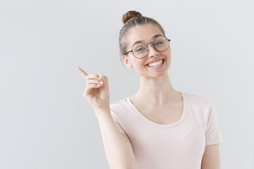 Indoor picture of optimistic European girl isolated on gray background in fashionable eyeglasses,...