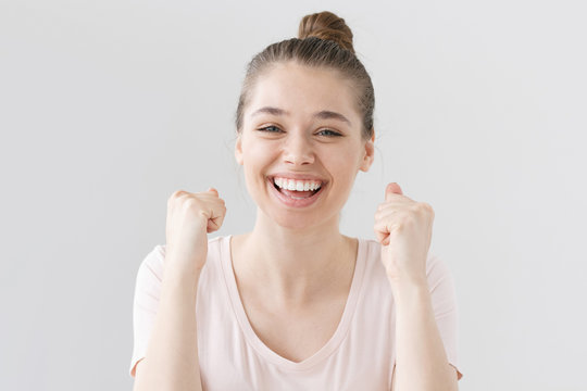 Indoor photo of good-looking teenage girl isolated on gray background celebrating victory and acting as if she is winner, squeezing fists in deep emotional expression of happiness, luck and content.