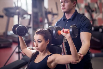 Tuinposter Personal trainer helping woman working with heavy dumbbells © alfa27