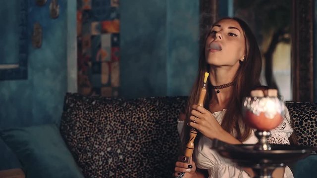 Young european woman in arabic style cafe smoking shisha then smiling, blue walls with ornament. Shot with sony a7s on a tripod