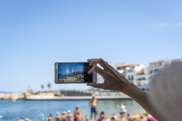 Hand held smartphone taking a picture in the beach of l'Escala. Costa Brava, Girona province, Spain.