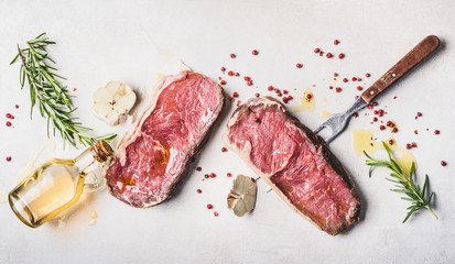 Raw beef Striploin steaks with oil , spices and meat fork on white stone background, top view, flat...