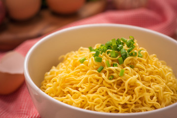 Instant noodles in bowl with vegetables on wood background