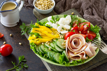 Salad with ham, fresh vegetables, pine nuts, arugula, mozzarella and salad dressing vinaigrette on a gray stone background or slate. Copy space.