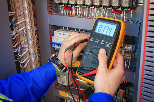 Electrical Engineer adjusts electrical equipment with a multimeter in his hand closeup.