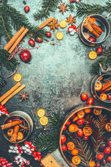 Christmas mulled wine background. Cooking pot and mugs with mulled wine, fir brunches, festive decoration and spices, top view, frame