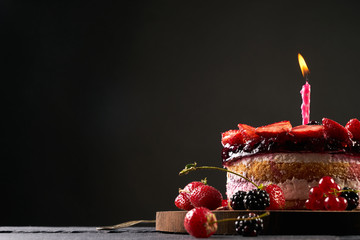 Wodden cake board with homemade raspberry-blackberry and strawberry birthday tart on dark stone...