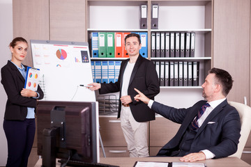 Boss pointing at the mistake on the flip chart at a meeting in office. Boss and his colleagues