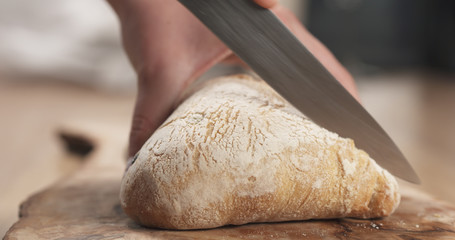 young female hands slicing ciabatta with olives on cutting board