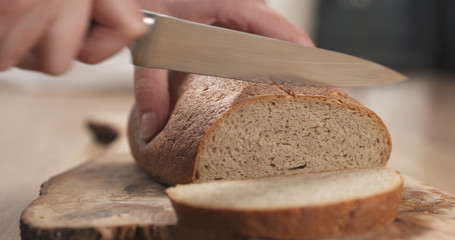 young female hands slicing rye wheat rustic bread on cutting board