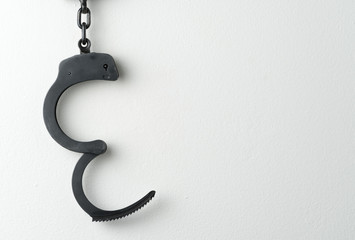 Metal police handcuffs on white painted wall with potential copy space
