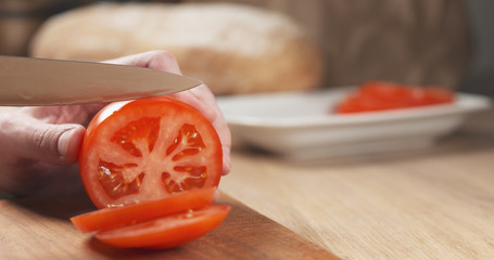 young man hands slicing tomato on cutting board