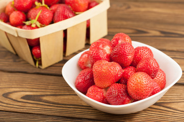 Fresh ripe strawberries in white bowl and wicker basket on rustic wooden planks