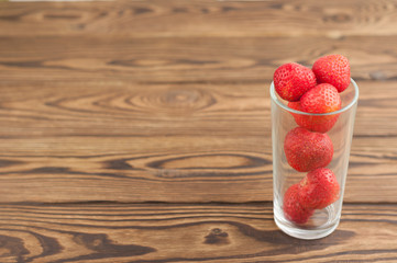 Ripe strawberries in glass on old wooden background