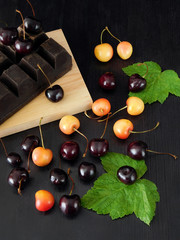 Two sorts of cherry are scattered on a dark table. Ruby and yellow cherries on a dark background