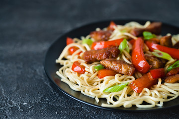 Szechuan stir fried spicy pork with red pepper and green onion. Chinese food or Asian cuisine concept on dark background. Selective focus