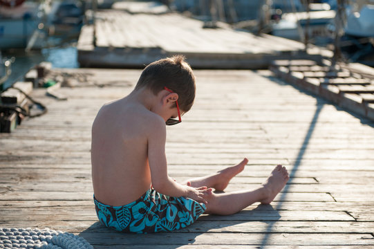 little kid sitting on wooden jetty in sunny summer day